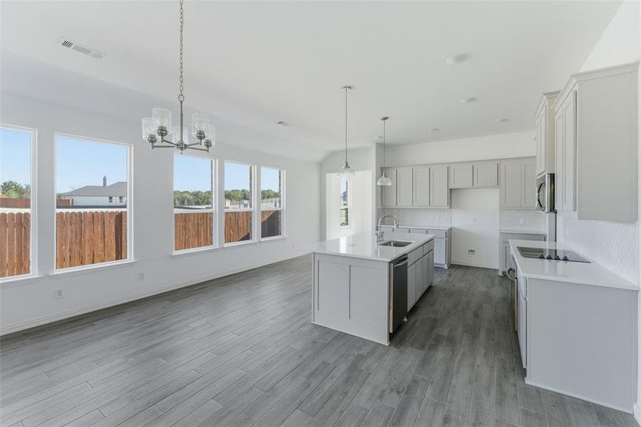 Kitchen with a center island with sink, hanging lights, white cabinetry, light stone countertops, and dark wood-type flooring