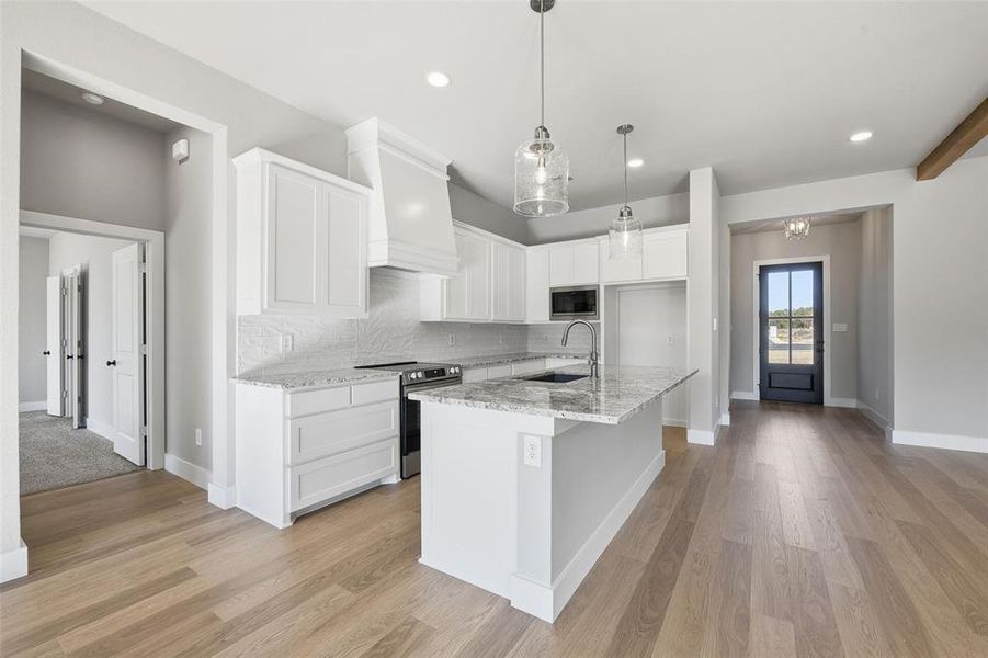 Kitchen featuring appliances with stainless steel finishes, tasteful backsplash, white cabinetry, light stone counters, and an island with sink Kitchen featuring appliances with stainless steel finishes, tasteful backsplash, white cabinetry, light stone counters, and an island with sink
