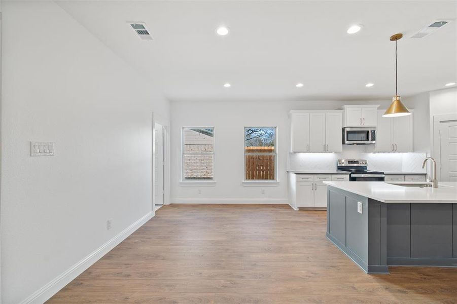 Kitchen with sink, hanging light fixtures, stainless steel appliances, white cabinets, and light wood-type flooring