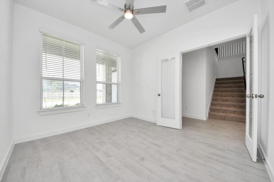 Experience the perfect blend of sophistication and warmth in this home office, boasting elegant wood-look tile flooring and flooded with natural light from expansive windows and French doors. Sample photo of completed home with similar floor plan. Actual colors and selections may vary.