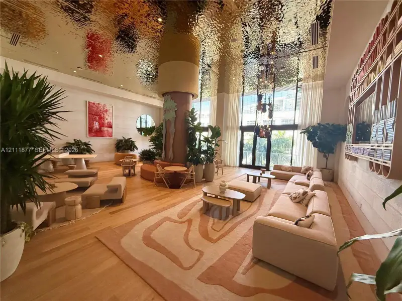 Common area featuring a reflective textured ceiling, floor-to-ceiling windows, wood-finish flooring, and a large built-in decorative shelving unit