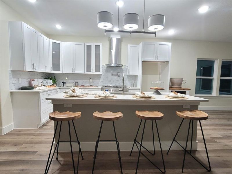 Kitchen with shaker soft closing white cabinets, stainless steel exhaust hood, a kitchen breakfast bar, 36 inch stove for gourmet chefs and an island with sink