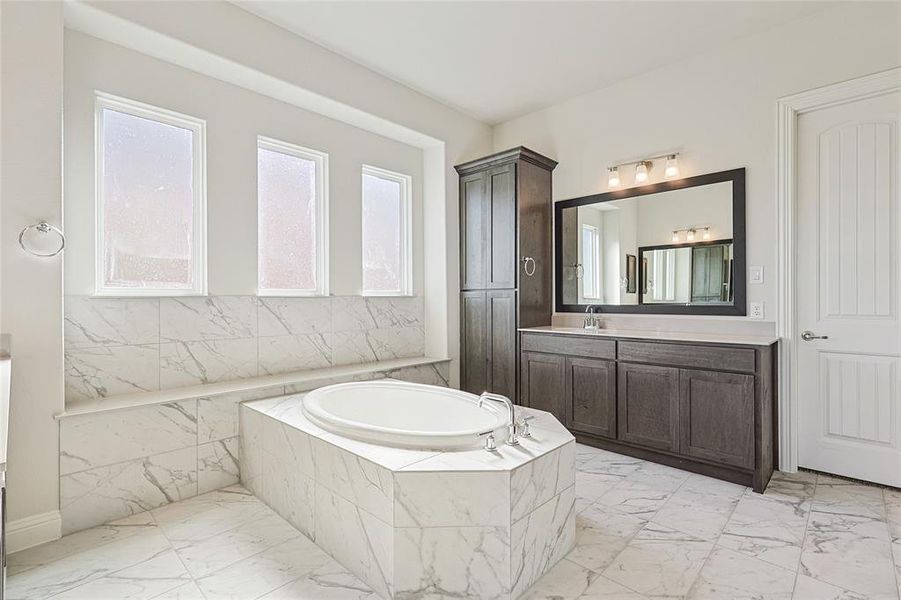 Full bath featuring vanity, light marble finish flooring, and a garden tub