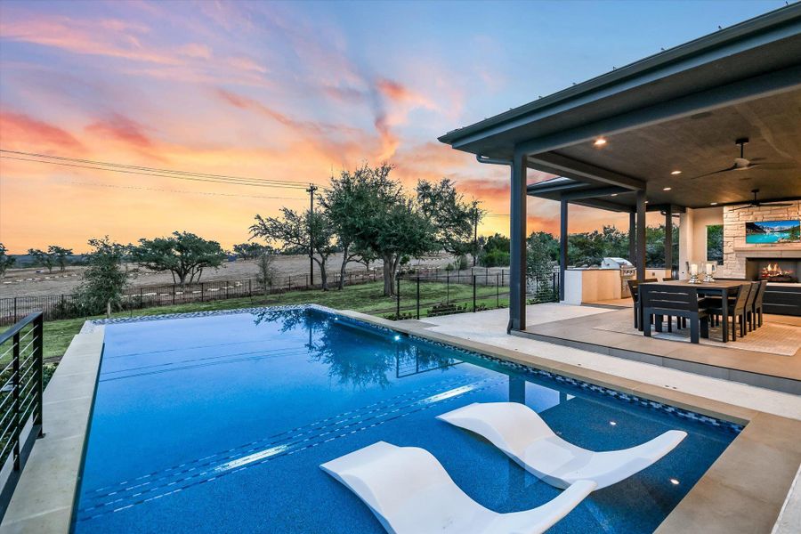 View of pool featuring patio surround, a fenced backyard, and an outdoor stone fireplace View of pool featuring patio surround, a fenced backyard, and an outdoor stone fireplace