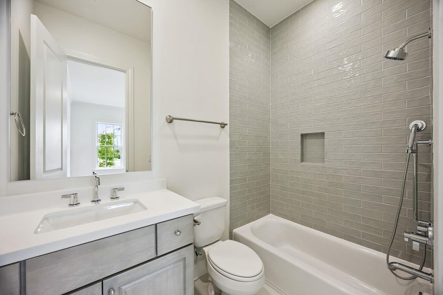 En-suite bath serving the first-floor secondary bedroom has tile to the ceiling and shampoo niche.