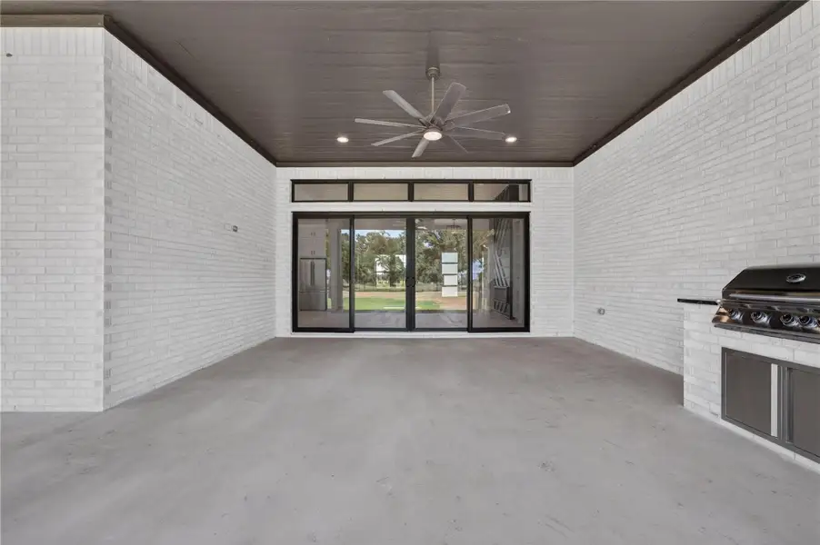 White brick walls enclose a covered outdoor living area featuring a built-in grill and concrete flooring.