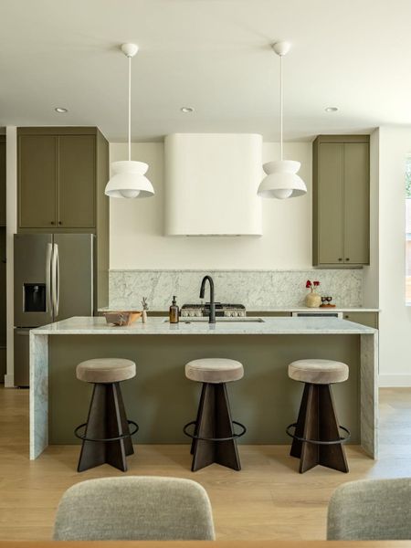 Marble waterfall island with bar seating and integrated cooktop anchors this modern culinary space.