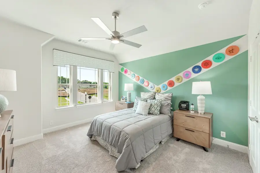 Bedroom with teal accent wall, ceiling fan, carpet, and colorful disc decorations arranged in a V pattern above the bed