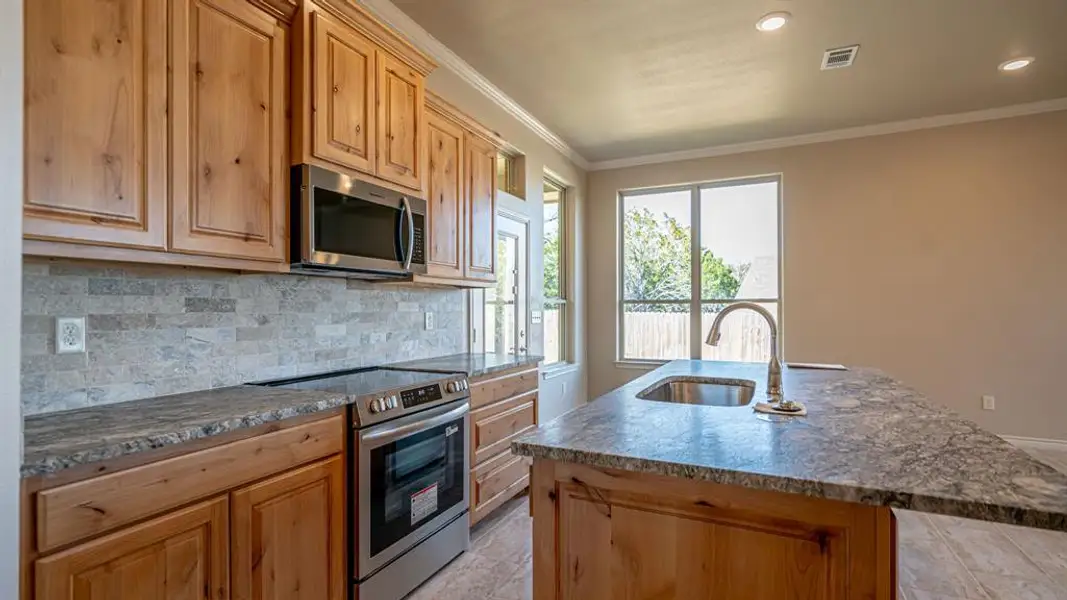 Kitchen with stainless steel appliances, an island with sink, dark stone counters, ornamental molding, and tasteful backsplash