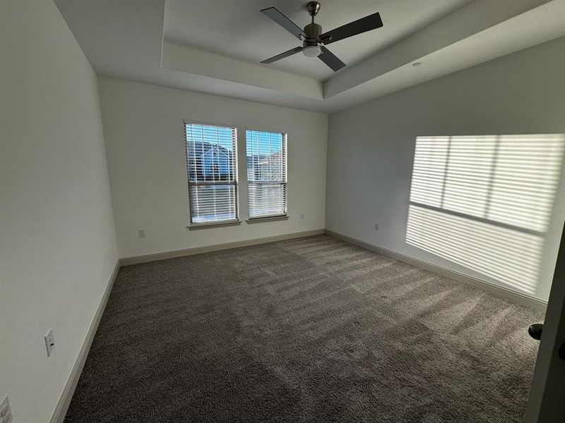 Carpeted empty room with a raised ceiling and ceiling fan