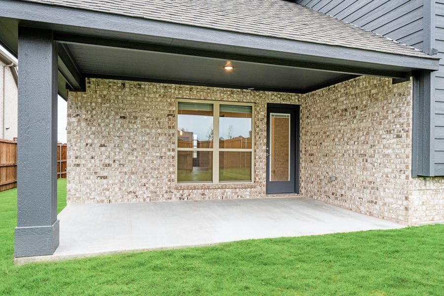 Covered back patio with concrete slab, brick exterior wall, large window, and black door overlooking green lawn Covered back patio with concrete slab, brick exterior wall, large window, and black door overlooking green lawn