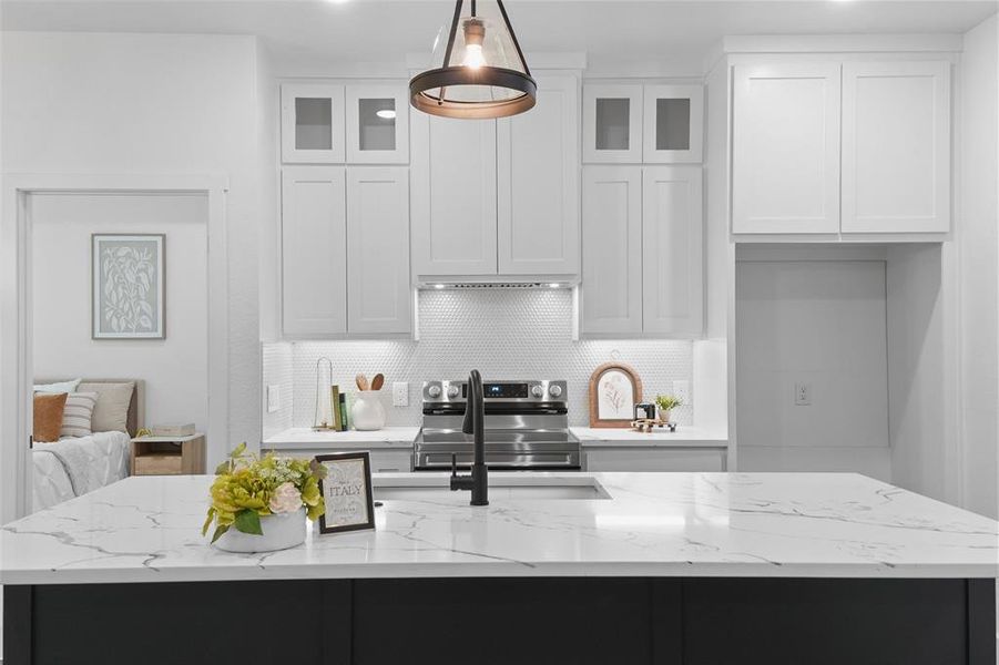 Kitchen island featuring a white countertop with grey veining, a matte black sink faucet, stainless steel range, white shaker-style cabinetry, and a white hexagonal tile backsplash Kitchen island featuring a white countertop with grey veining, a matte black sink faucet, stainless steel range, white shaker-style cabinetry, and a white hexagonal tile backsplash