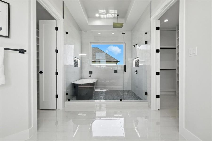 Full bath with a spacious closet, a shower stall, a soaking tub, a tray ceiling, and tile patterned floors Full bath with a spacious closet, a shower stall, a soaking tub, a tray ceiling, and tile patterned floors