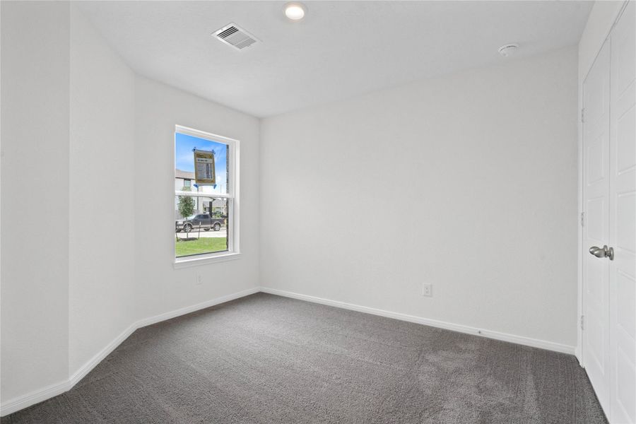 Tucked peacefully in the front of the home is this secondary bedroom which features plush carpeting, neutral paint, a large window, and a spacious closet.