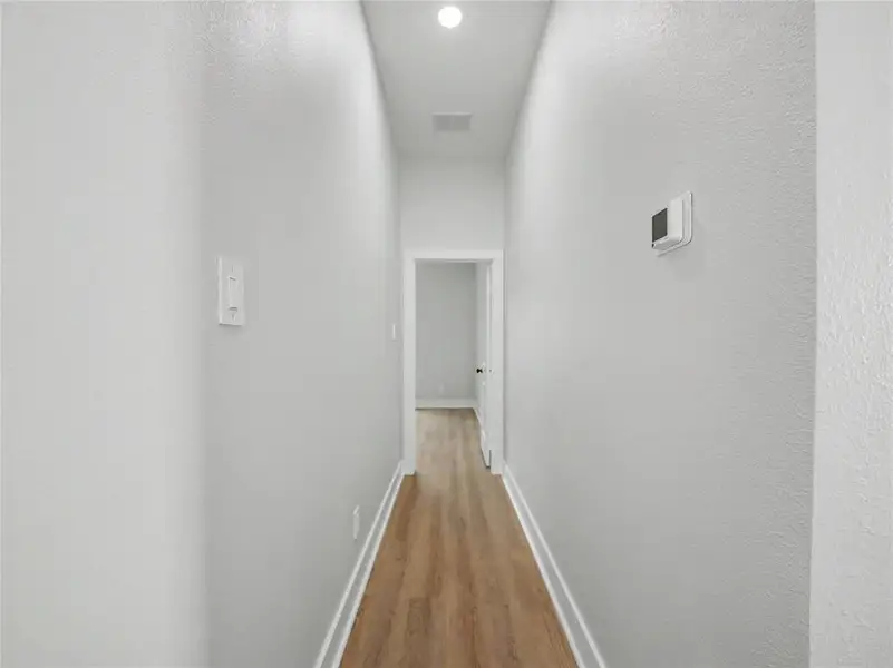 Hallway featuring wood-finish flooring, white baseboards, and light gray wall paint Hallway featuring wood-finish flooring, white baseboards, and light gray wall paint