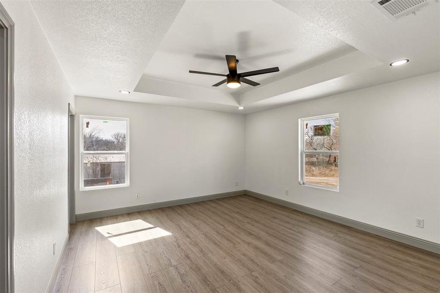 Empty room with a ceiling fan, light wood finished floors, a textured ceiling, recessed lighting, and a raised ceiling
