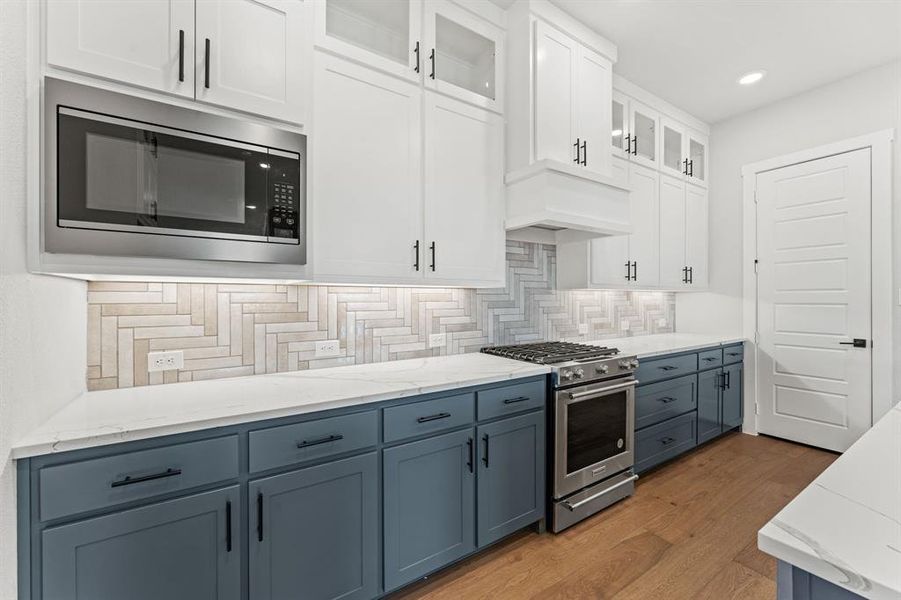 Kitchen with decorative backsplash, dark hardwood / wood-style flooring, custom range hood, stainless steel appliances, and white cabinets