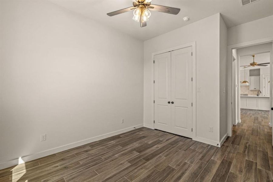Unfurnished bedroom featuring dark wood finished floors, a closet, baseboards, and ceiling fan