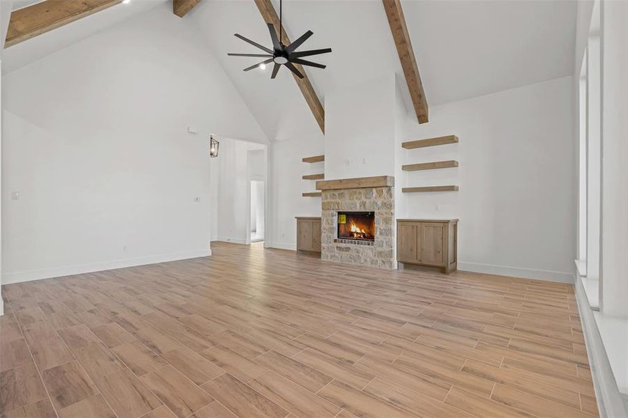 Unfurnished living room featuring high vaulted ceiling, a ceiling fan, a stone fireplace, beam ceiling, and wood finish floors