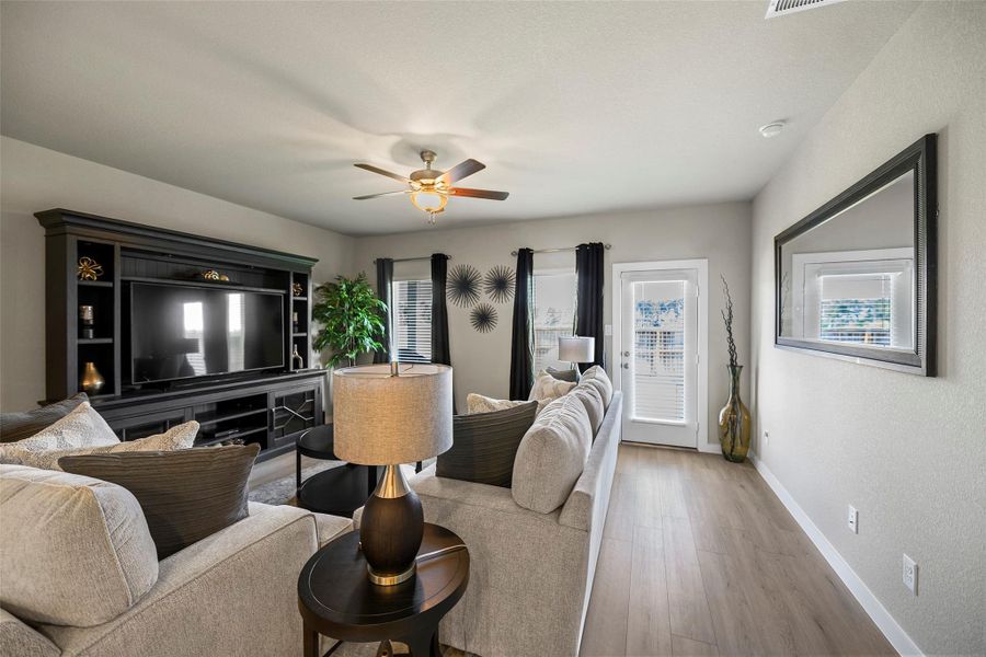 Spacious living room with elegant wood flooring.  Natural light streams through the windows, complementing the modern decor and ceiling fan.