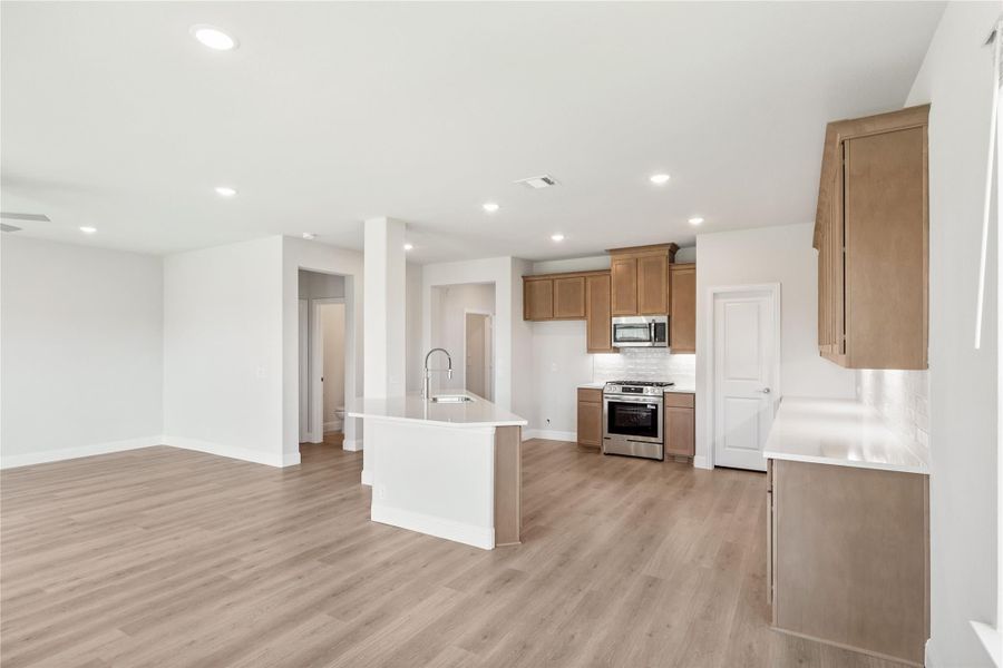 Open-concept kitchen with center island, brown cabinets, stainless steel appliances, and light wood floors