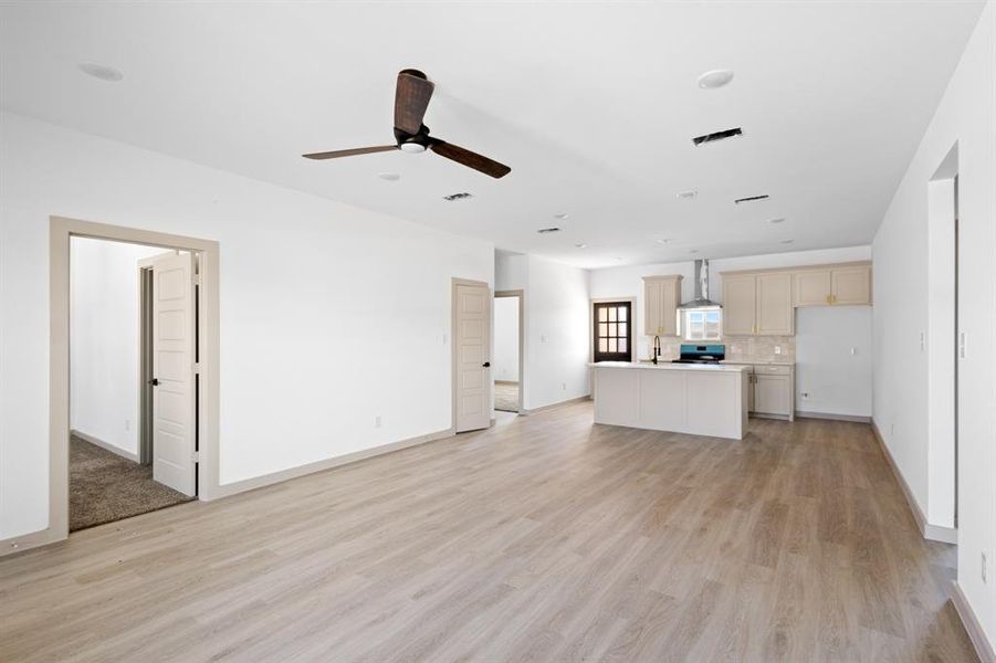 Unfurnished living room featuring baseboards, a ceiling fan, visible vents, and light wood-type flooring Unfurnished living room featuring baseboards, a ceiling fan, visible vents, and light wood-type flooring