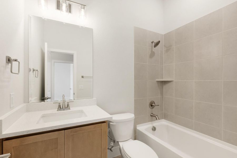 Full bathroom with single vanity, white countertop, toilet, and tiled shower-tub combo with brushed nickel fixtures Full bathroom with single vanity, white countertop, toilet, and tiled shower-tub combo with brushed nickel fixtures