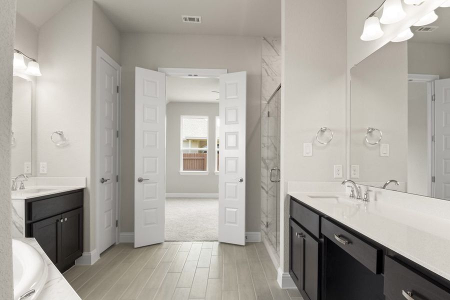 The primary bathroom with a glass shower with marble tiles, vanities with white countertops and dark brown cabinets, and vinyl flooring.