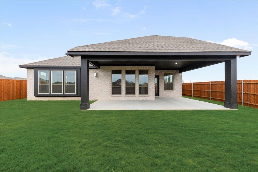 Rear exterior of single-story brick home with covered patio, concrete slab, and fenced backyard with green lawn Rear exterior of single-story brick home with covered patio, concrete slab, and fenced backyard with green lawn