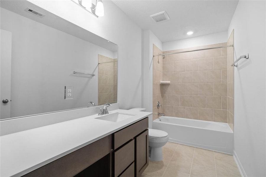 Secondary bath features tile flooring, tub/shower combo with tile surround, stained wood cabinets, beautiful light countertops, mirror, sleek fixtures and modern finishes.