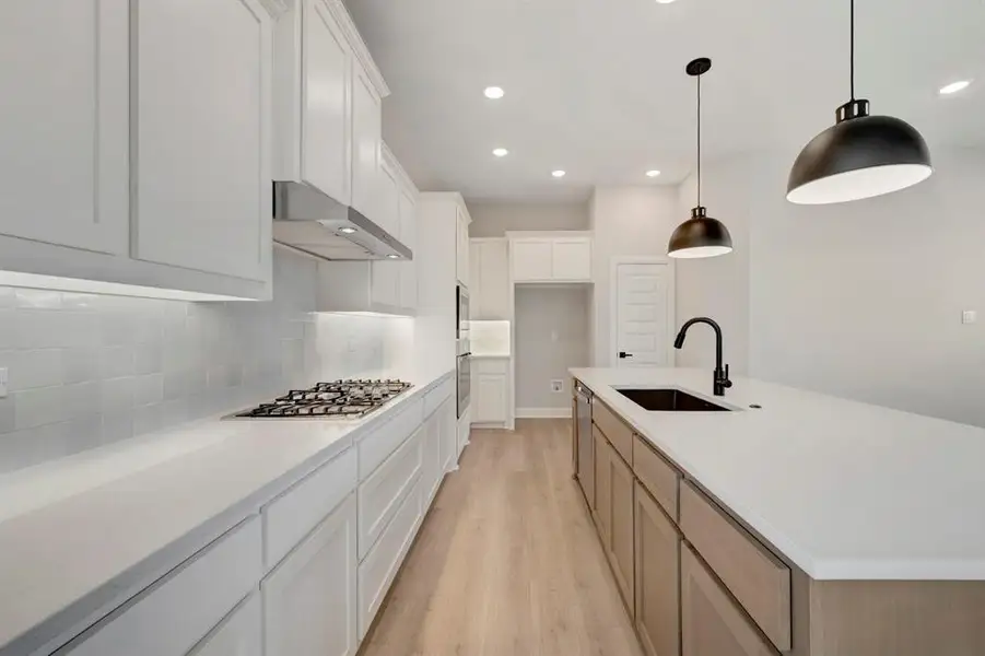 Kitchen with an island with sink, light wood finished floors, dual tone cabinets, decorative light fixtures, and stainless steel appliances
