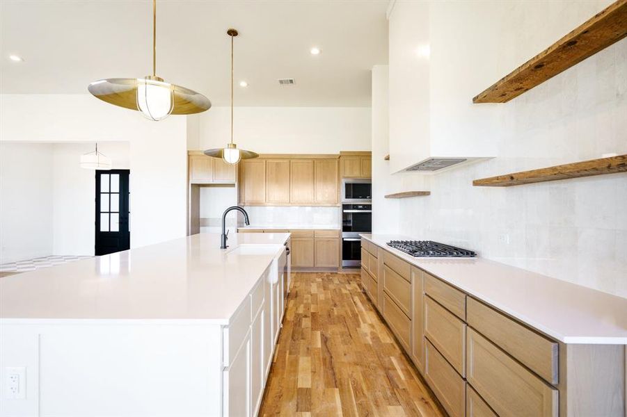 Kitchen featuring light wood-type flooring, stainless steel appliances, sink, a large island with sink, and hanging light fixtures