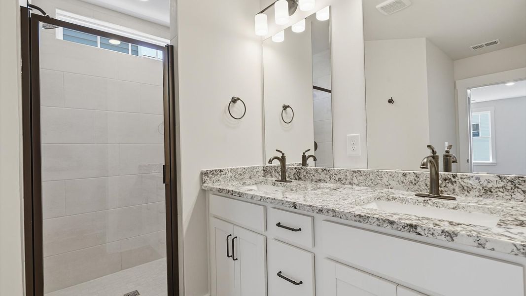Elegant primary bathroom featuring a spacious tiled walk-in shower and dual vanity in this first-class DRB Homes design Elegant primary bathroom featuring a spacious tiled walk-in shower and dual vanity in this first-class DRB Homes design