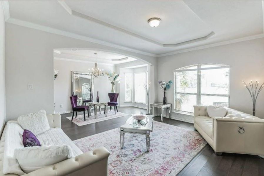 Living room featuring a tray ceiling, crown molding, an inviting chandelier, and dark hardwood / wood-style floors