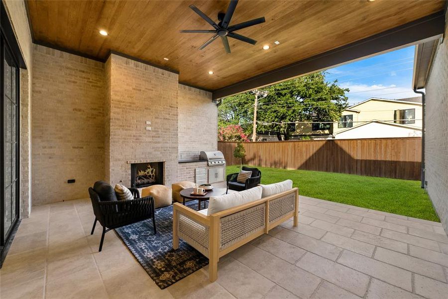 Covered outdoor patio featuring a wood-finish ceiling with recessed lighting and a ceiling fan, a brick fireplace, and an integrated outdoor kitchen