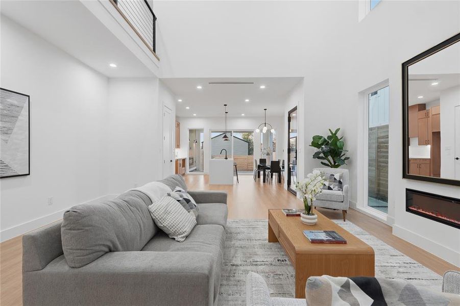 Living area with light wood-type flooring, a high ceiling, a glass covered fireplace, and recessed lighting