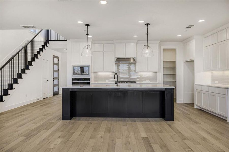 Kitchen with decorative backsplash, hanging light fixtures, a center island with sink, light wood-type flooring, and black oven