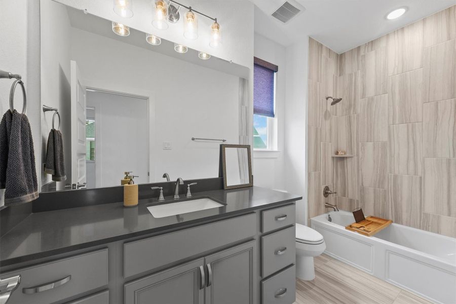 This secondary bathroom is well-appointed with a single vanity and stylish quartz countertops. It features a tub/shower combination with a beautiful tiled surround, providing a clean and modern look.