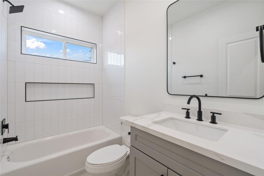 The secondary bathroom features a spacious shower with a large shampoo niche and tile that stretches all the way to the ceiling. This design adds both functionality and a sleek, modern look. It’s a stylish, practical space perfect for everyday use.