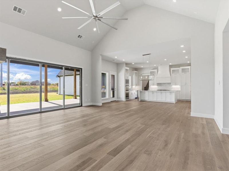 Unfurnished living room with high vaulted ceiling, recessed lighting, light wood finished floors, and a ceiling fan Unfurnished living room with high vaulted ceiling, recessed lighting, light wood finished floors, and a ceiling fan