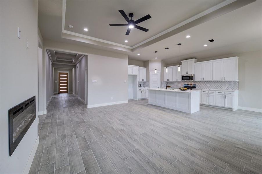 Kitchen featuring appliances with stainless steel finishes, a tray ceiling, an island with sink, and white cabinets