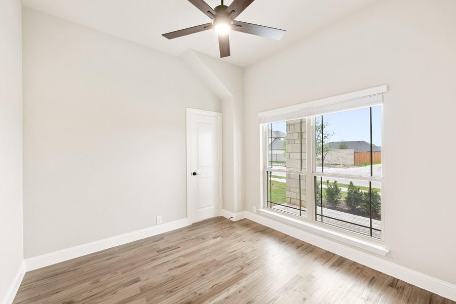 Empty bedroom with hardwood floors, ceiling fan, vaulted ceiling, and large window with neighborhood view Empty bedroom with hardwood floors, ceiling fan, vaulted ceiling, and large window with neighborhood view