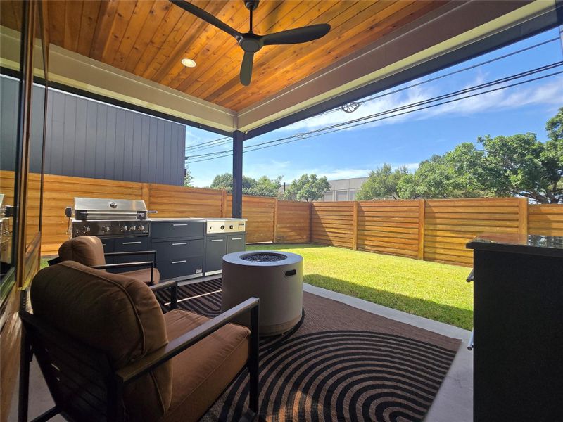 Rich wood plank ceilings shelter a concrete patio transitioning directly to a fenced grassy yard.