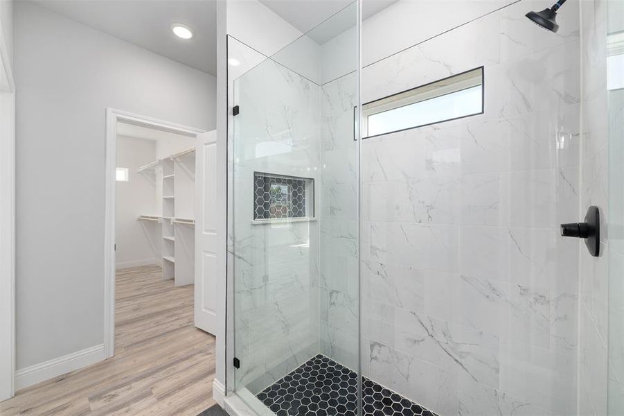 Full bathroom featuring baseboards, wood finished floors, a spacious closet, and tiled shower