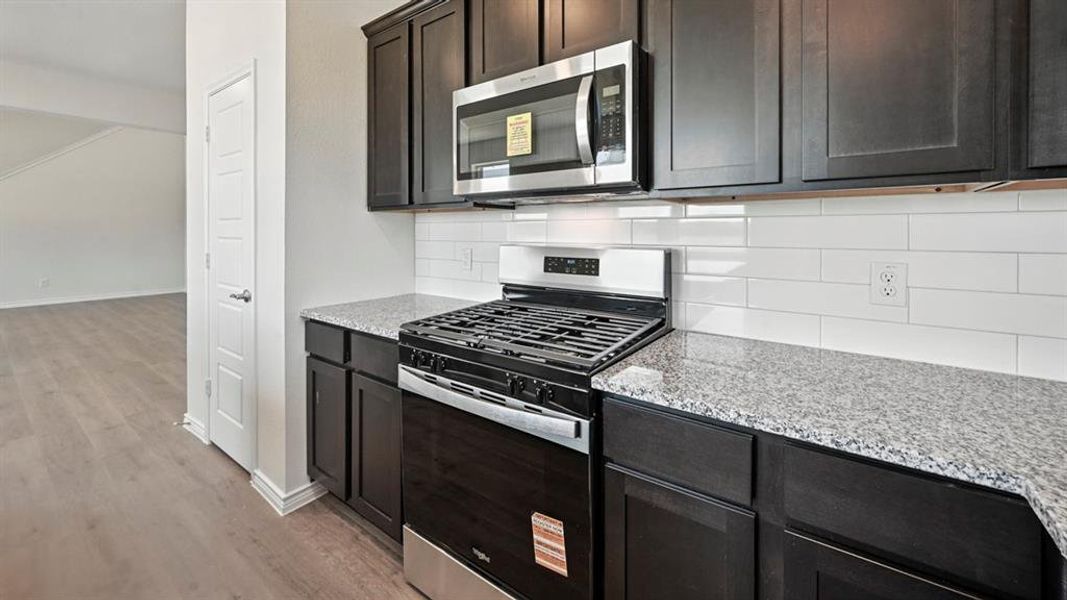 Kitchen with appliances with stainless steel finishes, decorative backsplash, light stone countertops, light wood-style floors, and dark brown cabinetry