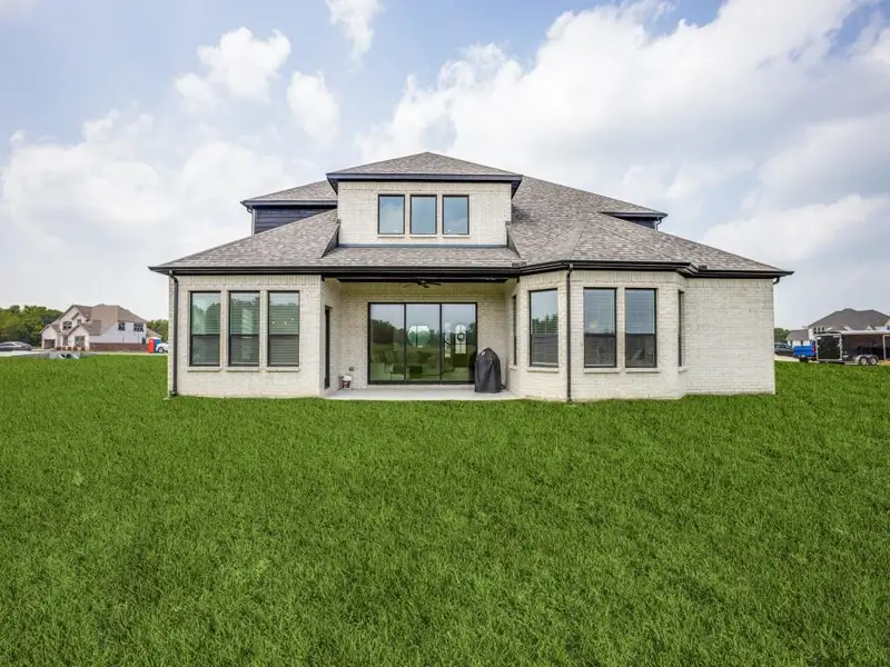 Back of property with brick siding, a shingled roof, a patio area, and a yard Back of property with brick siding, a shingled roof, a patio area, and a yard