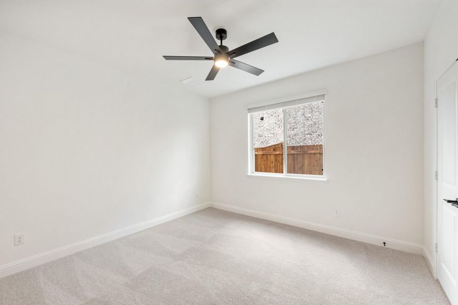 Empty bedroom with carpet flooring, ceiling fan, and single window with backyard view