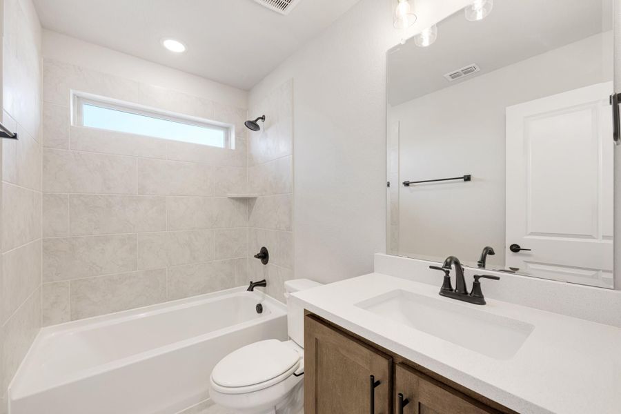 Bathroom with tiled tub-shower combo, wood vanity, white countertop, and matte black fixtures Bathroom with tiled tub-shower combo, wood vanity, white countertop, and matte black fixtures