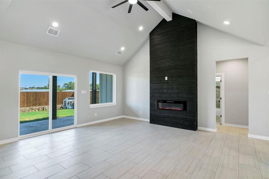 Unfurnished living room featuring beam ceiling, ceiling fan, high vaulted ceiling, light hardwood / wood-style floors, and a fireplace