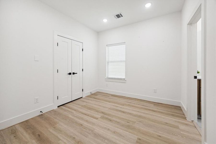 The spacious secondary bedroom features wood-look LVP flooring, recessed lighting, and a large window that fills the room with natural light